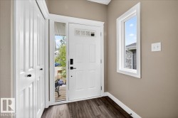 Entryway featuring a white paneled front door with a transom window and sidelight, wood-finish flooring, a full-length window, and a built-in closet with bifold doors - 