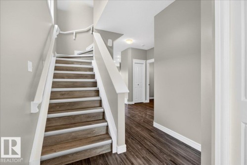 Staircase with wood-finish treads and white risers, featuring white handrails and painted walls - 62 Durrand Bend, Fort Saskatchewan, AB 