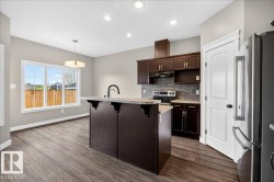 Kitchen and dining area featuring wood-finish flooring, dark wood cabinetry, a central island with a breakfast bar, stainless steel appliances, and a tiled backsplash - 