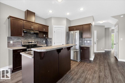 Kitchen featuring rich wood-finish cabinetry, stainless steel appliances, a tile backsplash, light-toned countertops, and wood-finish flooring - 62 Durrand Bend, Fort Saskatchewan, AB 