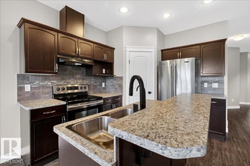 Contemporary kitchen featuring wood-finish cabinetry, granite-style countertops, and stainless steel appliances - 62 Durrand Bend, Fort Saskatchewan, AB 