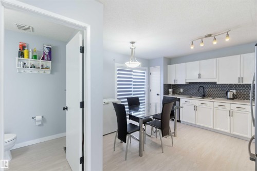 Kitchen with white cabinetry, dark hex tile backsplash, and light wood-finish flooring - 8 15128 22 Street, Edmonton, AB 