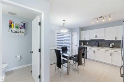 Kitchen with white cabinetry, dark hex tile backsplash, and light wood-finish flooring - 
