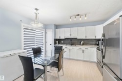 Modern kitchen featuring white cabinetry, a dark hexagonal tile backsplash, light wood-finish flooring, a stainless steel refrigerator, and a sliding glass door - 