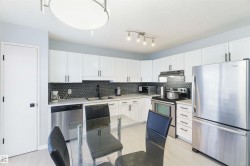 Modern kitchen featuring white cabinetry, a dark hexagonal tile backsplash, stainless steel appliances, light wood-finish flooring, and a contemporary ceiling light fixture - 