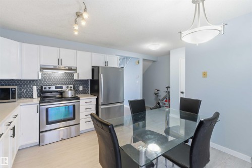Kitchen featuring white cabinetry with dark hardware, stainless steel appliances, a dark hexagonal tile backsplash, and light countertops - 8 15128 22 Street, Edmonton, AB 