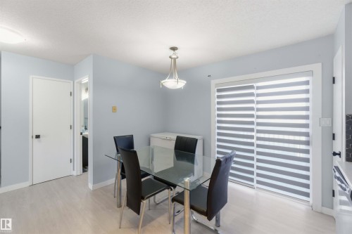 Dining area featuring light wood-finish flooring, a contemporary ceiling fixture, and a sliding glass door with horizontal blinds - 8 15128 22 Street, Edmonton, AB 
