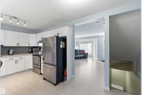Kitchen featuring white cabinetry with dark hardware, dark hexagonal tile backsplash, light countertops, and stainless steel appliances - 8 15128 22 Street, Edmonton, AB 