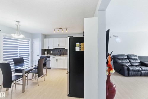Open-concept dining area featuring light wood-finish flooring, a contemporary overhead light fixture, and horizontal window blinds - 8 15128 22 Street, Edmonton, AB 