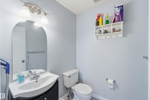 Bathroom featuring a curved vanity with integrated sink, arched wall mirror, and a two-light vanity fixture - 8 15128 22 Street, Edmonton, AB 