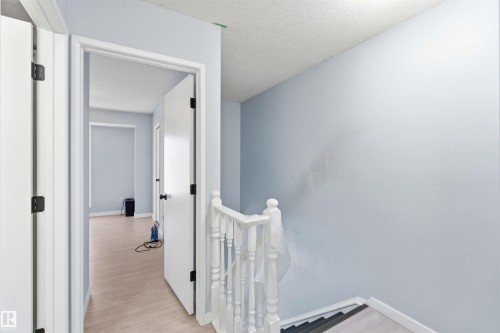 Hallway featuring light wood-finish flooring, white doors with black hardware, and a white staircase railing with white balusters - 8 15128 22 Street, Edmonton, AB 