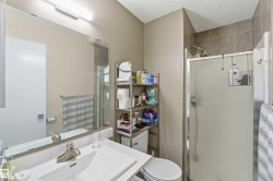 Bathroom featuring a vanity with an integrated sink, a large wall-mounted mirror, overhead bar lighting, a commode, and a shower enclosure with a tiled surround - 