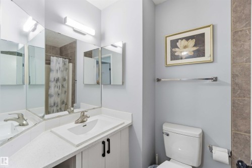 Bathroom featuring a single vanity with an integrated sink, a large wall-mounted mirror, and white cabinetry with black hardware - 8 15128 22 Street, Edmonton, AB 
