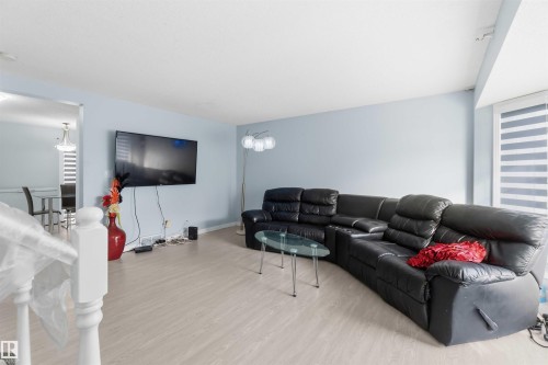 Open-concept living area featuring light wood-finish flooring, a wall-mounted television, and neutral blue wall tones - 8 15128 22 Street, Edmonton, AB 