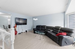 Open-concept living area featuring light wood-finish flooring, a wall-mounted television, and neutral blue wall tones - 