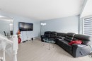 Open-concept living area featuring light wood-finish flooring, a wall-mounted television, and neutral blue wall tones - 8 15128 22 Street, Edmonton, AB 