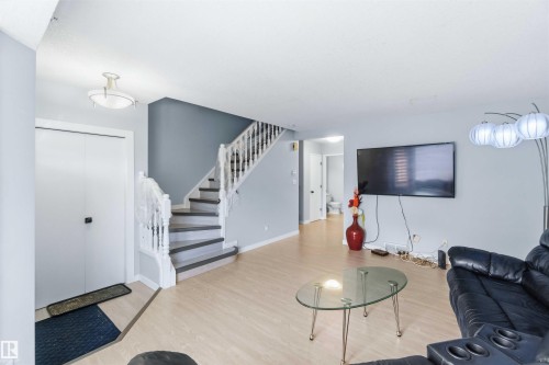 Open-concept living area featuring light wood-finish flooring, a white spindle staircase with dark treads, and a white bi-fold door - 8 15128 22 Street, Edmonton, AB 