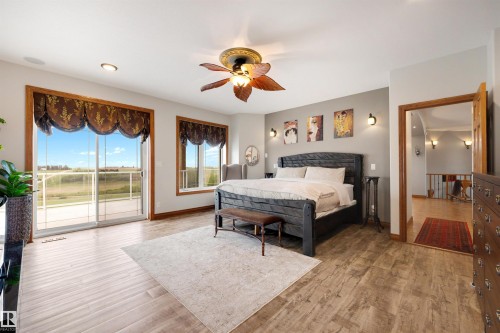 Spacious bedroom featuring wood-finish flooring, a ceiling fan with integrated lighting, and multiple windows - 28125 Highway 587, Rural Red Deer County, AB 