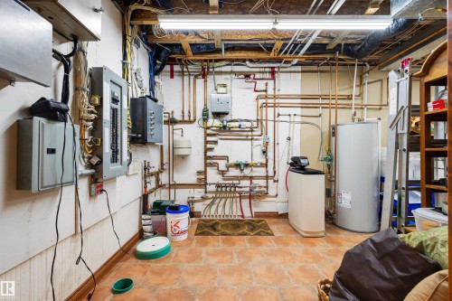 Utility room featuring exposed ceiling joists, overhead strip lighting, multiple electrical panels, extensive copper piping, and a water heater - 28125 Highway 587, Rural Red Deer County, AB 