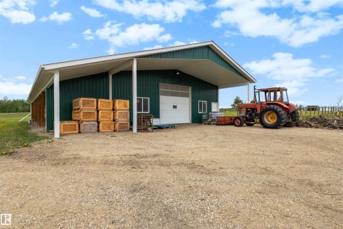 Green metal building with a white overhead door, an extended white covered overhang, and a gravel foreground - 28125 Highway 587, Rural Red Deer County, AB 