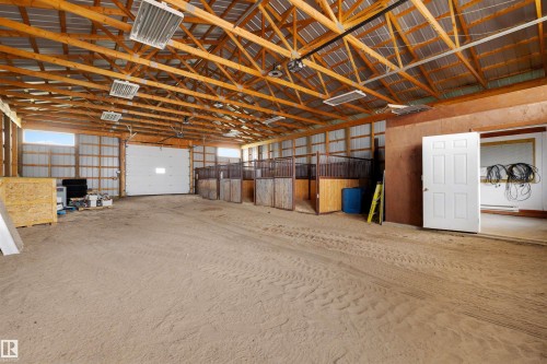 Spacious interior barn with exposed wood beam ceiling, multiple stalls, large roll-up door, and extensive open floor area - 28125 Highway 587, Rural Red Deer County, AB - Indoor