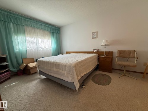 Carpeted room featuring a large window with sheer and opaque curtains, a light-colored wall, and a textured ceiling - 102 4610 50 Avenue, Stony Plain, AB 