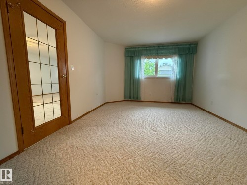Window with light blue drapes and valance, light-toned patterned carpeting, white walls, and a wood-finish door with glass panels - 102 4610 50 Avenue, Stony Plain, AB 