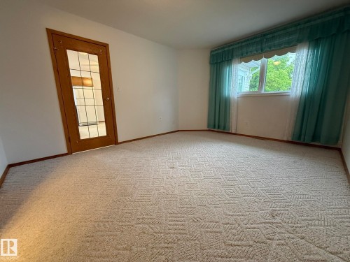 Spacious room featuring patterned carpet flooring, white walls, and wood-finish baseboards - 102 4610 50 Avenue, Stony Plain, AB 