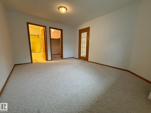 Spacious room featuring light-colored patterned carpeting, white walls, and wood trim - 102 4610 50 Avenue, Stony Plain, AB 