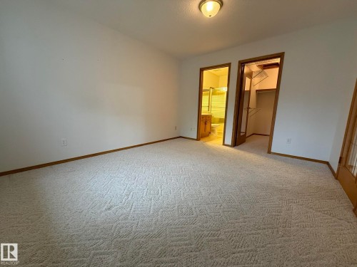 Spacious room featuring patterned carpet, white walls, wood trim, a ceiling-mounted light fixture, and two doorways - 102 4610 50 Avenue, Stony Plain, AB 