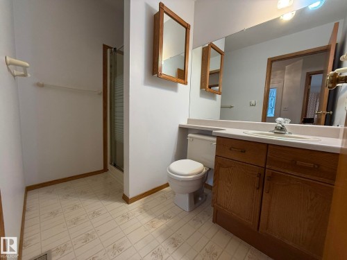 Bathroom featuring a vanity with a white countertop and wood-finish cabinetry, a built-in mirror, and a standing shower with a glass enclosure - 102 4610 50 Avenue, Stony Plain, AB 