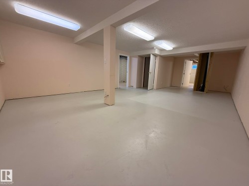Spacious lower-level room featuring light-toned walls and painted concrete flooring - 102 4610 50 Avenue, Stony Plain, AB 