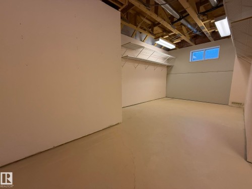 Unfinished interior space featuring exposed ceiling joists, overhead lighting, and a basement window - 102 4610 50 Avenue, Stony Plain, AB 