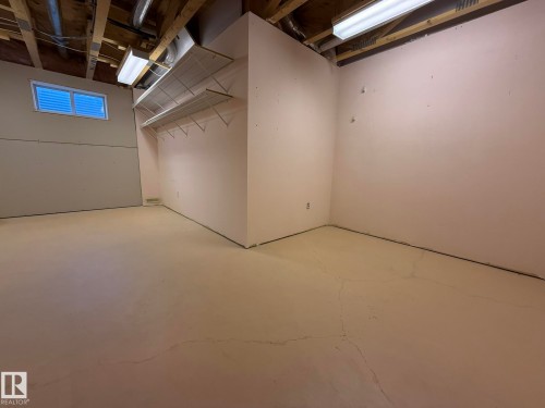 Unfinished basement space featuring exposed ceiling joists and ductwork, a small rectangular window, and an integrated wire shelving unit - 102 4610 50 Avenue, Stony Plain, AB 