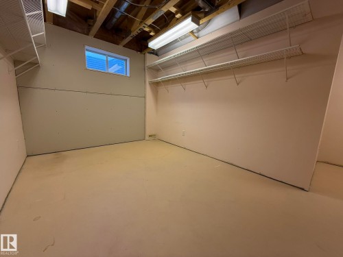 Unfinished room with exposed ceiling joists and overhead fluorescent lighting - 102 4610 50 Avenue, Stony Plain, AB 