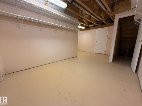 Open basement area featuring painted concrete flooring, exposed ceiling joists, and a white wire shelving system - 102 4610 50 Avenue, Stony Plain, AB 