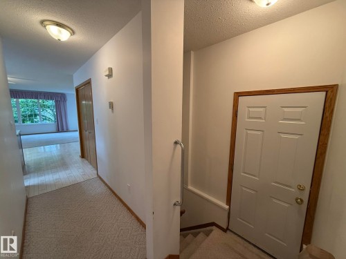 Interior hallway featuring a blend of carpet and wood-finish flooring, white walls, and a white six-panel door with wood trim - 102 4610 50 Avenue, Stony Plain, AB 
