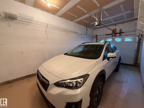 Attached garage featuring a light brown floor finish, white walls, and exposed ceiling joists - 102 4610 50 Avenue, Stony Plain, AB 