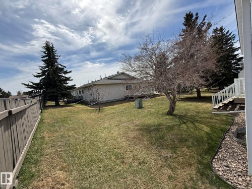 Expansive rear yard featuring a large mature conifer, established deciduous tree, manicured lawn, and wooden privacy fencing - 102 4610 50 Avenue, Stony Plain, AB 