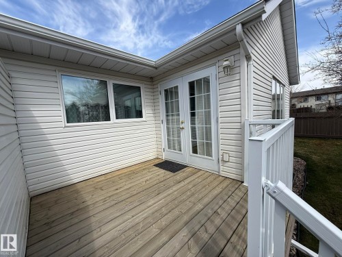 Expansive wood deck with white railing, featuring French doors with full-length glass panes, and white vinyl siding - 102 4610 50 Avenue, Stony Plain, AB 