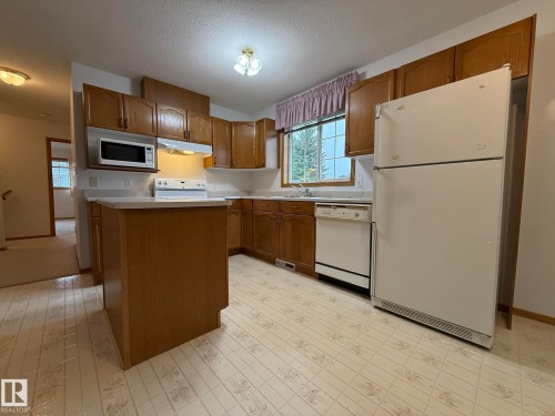 Kitchen with wood cabinetry, light countertops, and patterned vinyl flooring - 102 4610 50 Avenue, Stony Plain, AB 