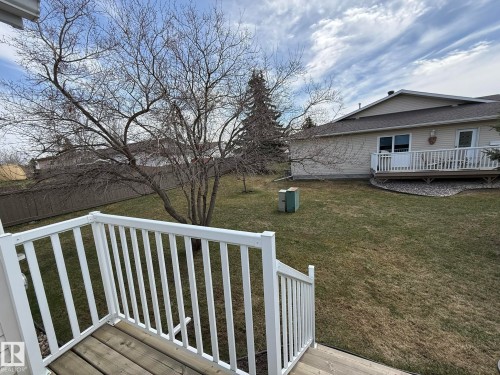 Spacious backyard featuring a sloped lawn, mature trees, and a privacy fence - 102 4610 50 Avenue, Stony Plain, AB 