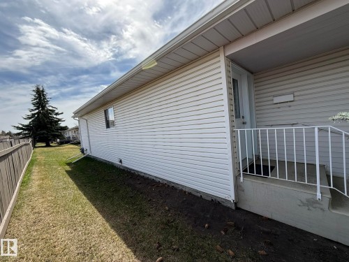 Exterior features include white vinyl siding, a covered entry with white railings, and a side yard with mature landscaping - 102 4610 50 Avenue, Stony Plain, AB 