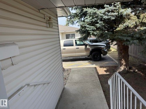Exterior entry with a white metal railing, concrete walkway, and gravel landscaping - 102 4610 50 Avenue, Stony Plain, AB 