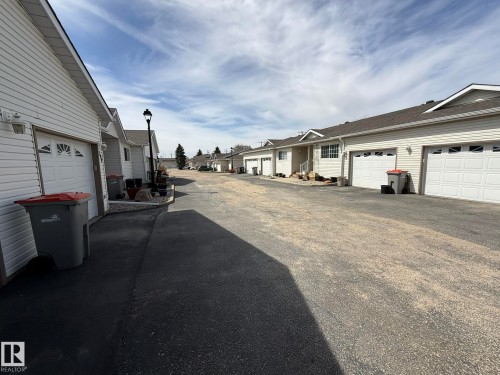 Row of residential units featuring white siding and individual attached garages - 102 4610 50 Avenue, Stony Plain, AB 