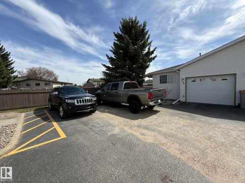 White vinyl siding exterior featuring an attached garage with a white panel door - 102 4610 50 Avenue, Stony Plain, AB 