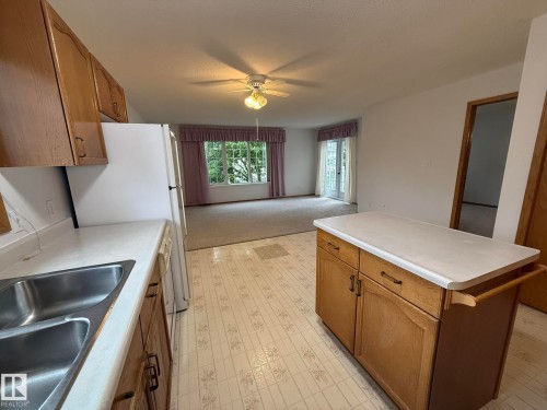 Kitchen area with light wood-finish cabinetry, white countertops, and a double stainless steel sink - 102 4610 50 Avenue, Stony Plain, AB 
