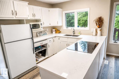 Kitchen featuring white cabinetry, light countertops, a double basin sink, and a built-in cooktop - 61 Stang Cres, Rural Two Hills County, AB 