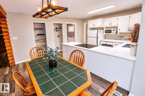 Open-concept kitchen and dining area featuring wood-finish flooring, white cabinetry with beadboard detailing, light-toned countertops, and a built-in cooktop - 61 Stang Cres, Rural Two Hills County, AB 