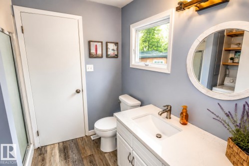Bathroom featuring a white vanity with an integrated sink and brushed nickel faucet, wood-finish flooring, a white-framed window, and a white toilet - 61 Stang Cres, Rural Two Hills County, AB 